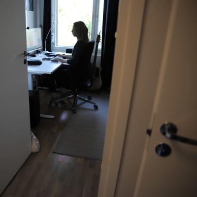 Nainen tekee kotonaan töitä tietokoneella. Naisesta näkyy siluetti ikkunaa vasten.