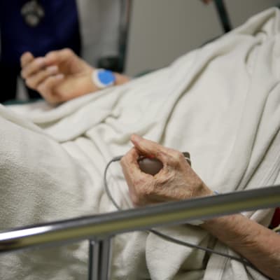 Sairaalasängyssä makaavan ikäihmisen kädet. 