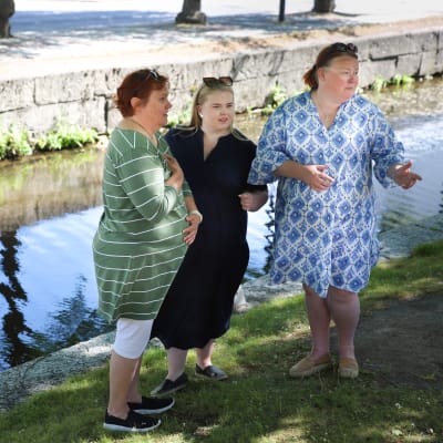Kolme naista seisoo kanaalin edessä kanaalin naispatsaita esittävissä asennoissa.