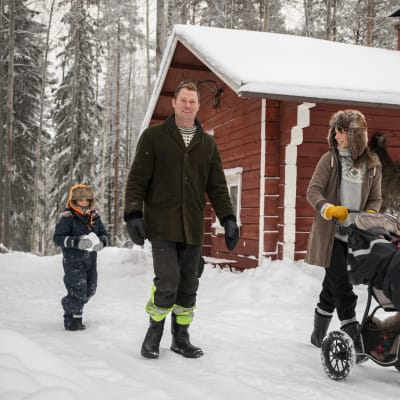 En vinterklädd familj framför en röd liten byggnad.