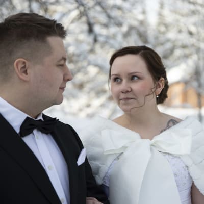 Hääpari katsoo toisaan silmiin lumisessa maisemassa.