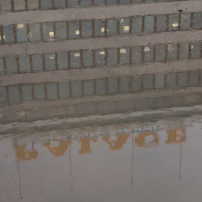 EK:s fasad speglar sig i en grå vattenpöl i regn.