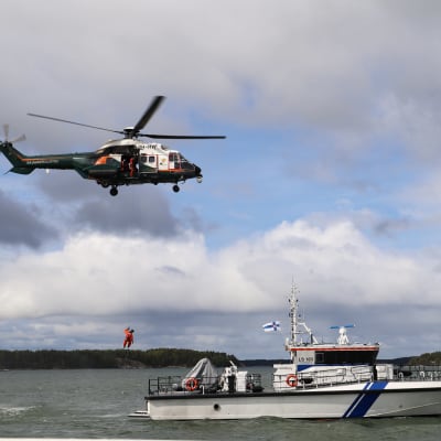 En person vinchas ner från sjöbevakningens helikopter i en patrullbåt. 