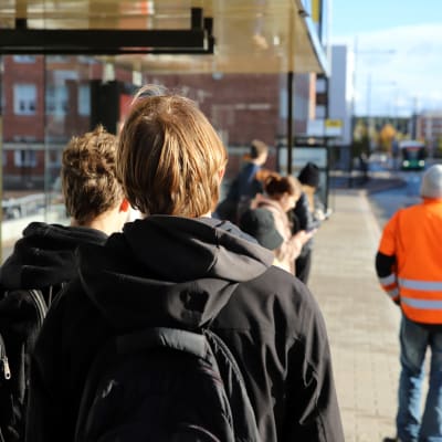 Unga personer står vid busshållplats.
