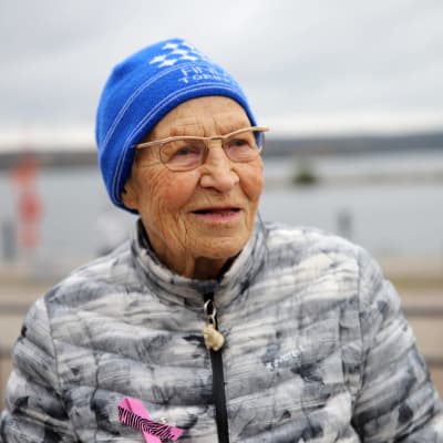 Siiri Rantanen istuu penkillä pipo päässä Vesijärven satamassa, järvi taka-alalla.