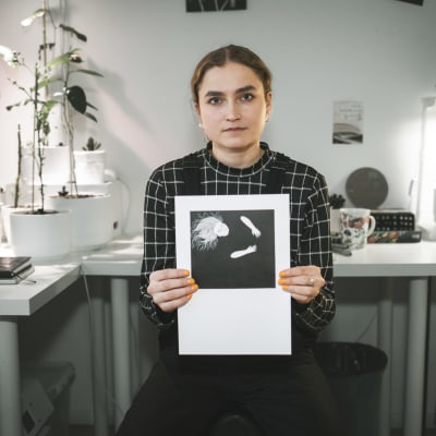 Emilia Laatikainen katsoo suoraan kameraan ja pitää käsissään piirtämäänsä kuvaa itsestään.