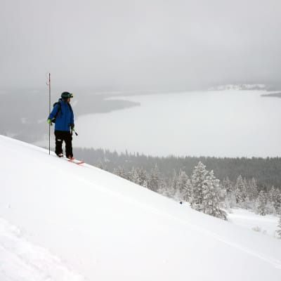 En man på skidor står i en snöklädd sluttning.