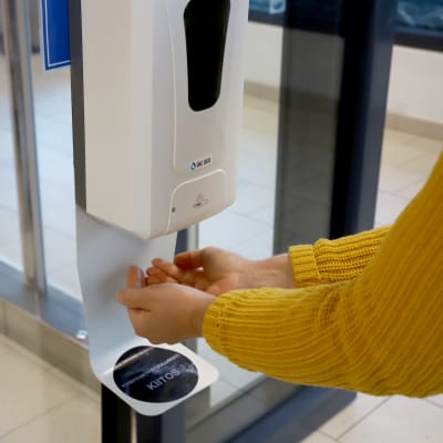 Två händer under en automat som doserar handsprit. 