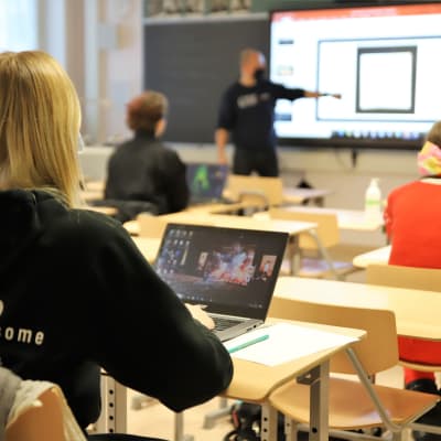 Abiturienter sitter i ett klassrum och lyssnar på en lärare som pekar på något.