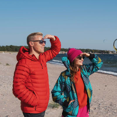 Egenandin juontajat Nicke Aldén ja Hannamari Hoikkala katselevat aurinkoisena päivänä Tulliniemen rannan purje- ja leijalautailijoita.