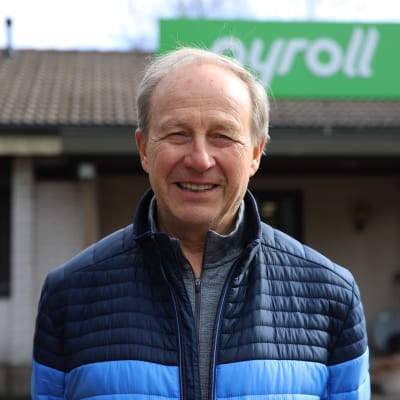 En äldre man tittar in i kameran och ler.