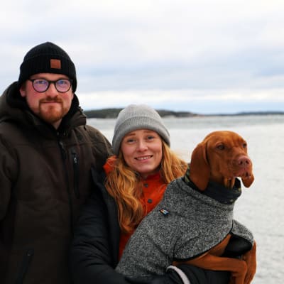 Simon Strömsund och Ida Törnroos står på en strand tillsammans med sin hund. 