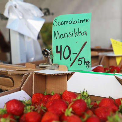 En papplåda med inhemska jordgubbar. En skylt med kilopris på en låda jordgubbar. 