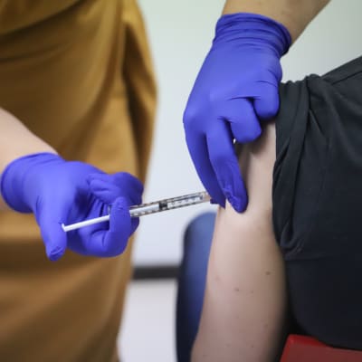 En persons arm blir stucken med en spruta med vaccin. 