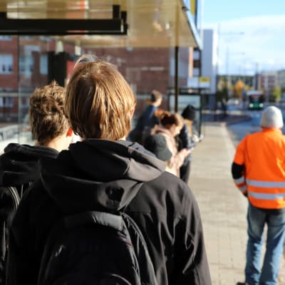 Unga personer står vid busshållplats.