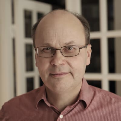 En man i röd skorta står i ett vitt rum. 