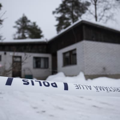 Polisen avspärrningsband framför ett vitt tegelhus. 