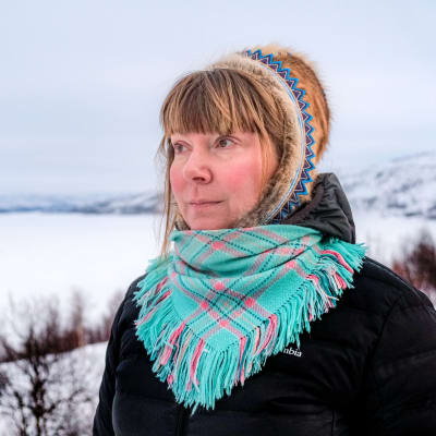 Kvinna står i samisk huvudbonad med Tana älv och fjäll i bakgrunden.