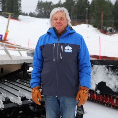 En man med grått hår och en mörkblå jacka står ute i vintrigt landskap.