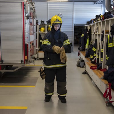 Anjalan VPK:n sopimuspalokuntalainen Jutta Tiitinen pukemassa pelastusalan vaatetusta päälle.