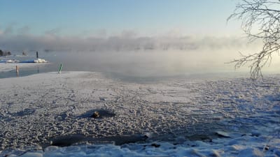 Isen lägger sig utanför Kitö bro i Sibbo skärgård, Kalvön i Borgå skärgård skymtar bakom sjöröken