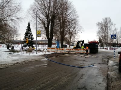Avstängd väg i Ingå kyrkby. Stängsel, grävmaskin och lastbil på vägen och en lekpark till vänster om vägen.