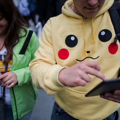 Två ungdomar spelar mobilspel. Den unga mannen bär en Pokémon Go-tröja.