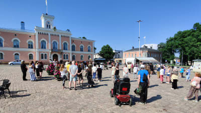 Människor står i solskenet på Lovisa torg.