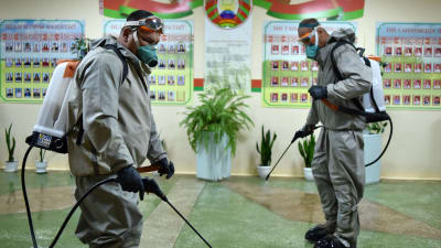 Två vitryska soldater i skyddsdräkr sprutar desinfektionsmedel i en skola