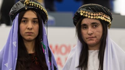 Nadia Murad till vänster, Lamiyja Aji Bashar till höger. De är klädda i yazidiernas traditionella dräkt med en slköja över huvudet samt ovanpå en hatt med guldslantar sydda runt brättet.