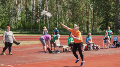 Nainen heittää urheilukentällä liitosaapasta, taustalla ihmisiä katsomassa.