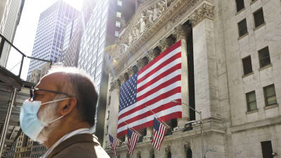En man i munskydd står utanför en byggnad i New York. I bakgrunden syns flaggor, USA:s flagga.