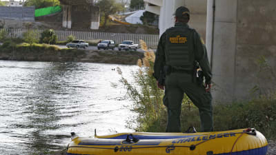 En gränskontrollant vid floden Rio Grande - i förgrunden en gummibåt som migranter tros ha använt för att ta sig över gränsen.