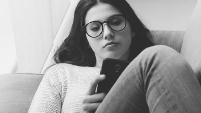 ledsen flicka sitter med en mobiltelefon i handen