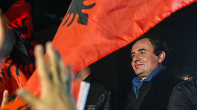 Vetevendosjes partiledare, valsegraren Albin Kurti står bland flaggor och ser ut att vara redo att hålla ett framförande. 