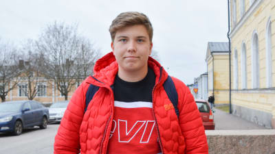 Tonåring i röd jacka utanför skola.