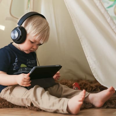 Pieni lapsi kuulokkeet korvilla tutkii älylaitetta.