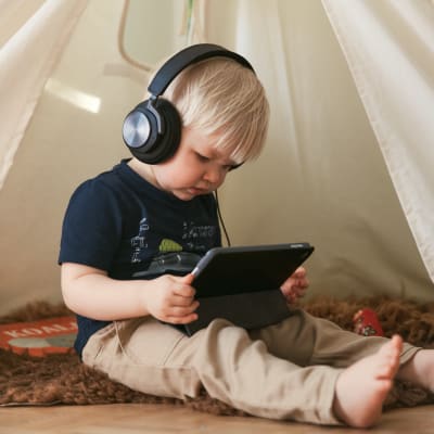Pieni lapsi kuulokkeet korvilla tutkii älylaitetta.