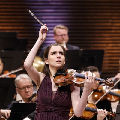 Armenialainen viulisti Diana Adamyan soittaa orkesterin edessä katse suunnattuna yläviistoon ja jousikäsi kohotettuna.