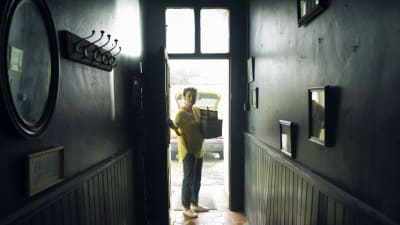 Grace (Katherine Walker) står vid en ytterdörr och ser in mot en mörk korridor.