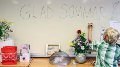 Skolelev skriver "glad sommar" på en tavla i skola.