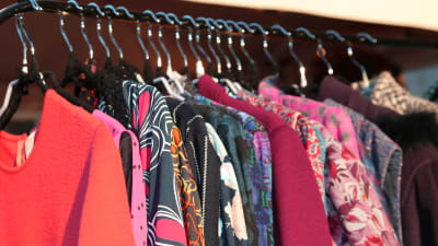 Färggranna kläder i vintagestil hänger på klädgalgar på ett kläräcke.
