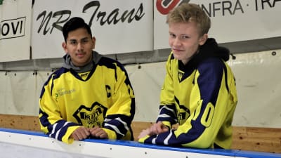 Lucas Nordgren och Linus Böling, hockeyspelare i Närpeslaget Krafts C-juniorer, står i ishallen vid sargen i gula spelskjortor