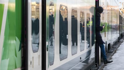 En person håller på att stiga ut ur ett tåg.