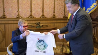 Ukrainas president Petro Porosjenko håller upp en t-skjorta med en bild av den fängslade Oleg Semtsov inför den brittiska musikern Elton John i Kiev i september 2015. 