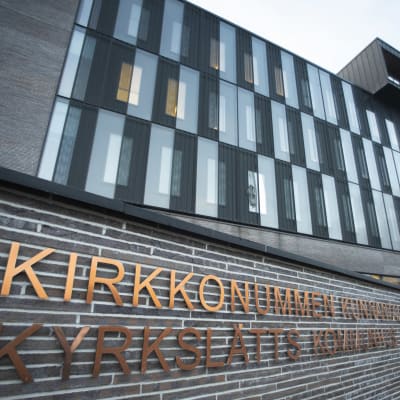 En skylt med texten "Kyrkslätts kommunhus". I bakgrunden en futuristisk grå byggnad. 