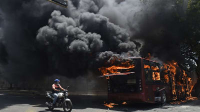 En oppositionsanhängare passerar en brinnande buss under gårdagens kravaller i Caracas