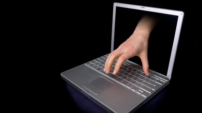 en bildbehandlad bild där en hand sticker ut ur en laptops skärm - bakgrunden är helt svart