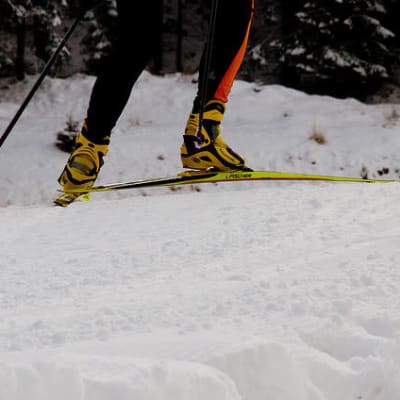 Lähikuvassa hiihtäjän jalat ja sukset lumella.