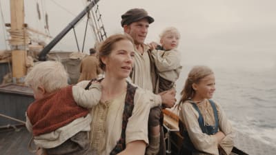 En familj står vid relingen till ett gammalt segelfartyg och tittar ut över havet.